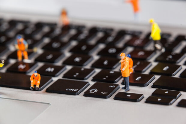 Conceptual image of miniature workmen repairing a laptop keyboard